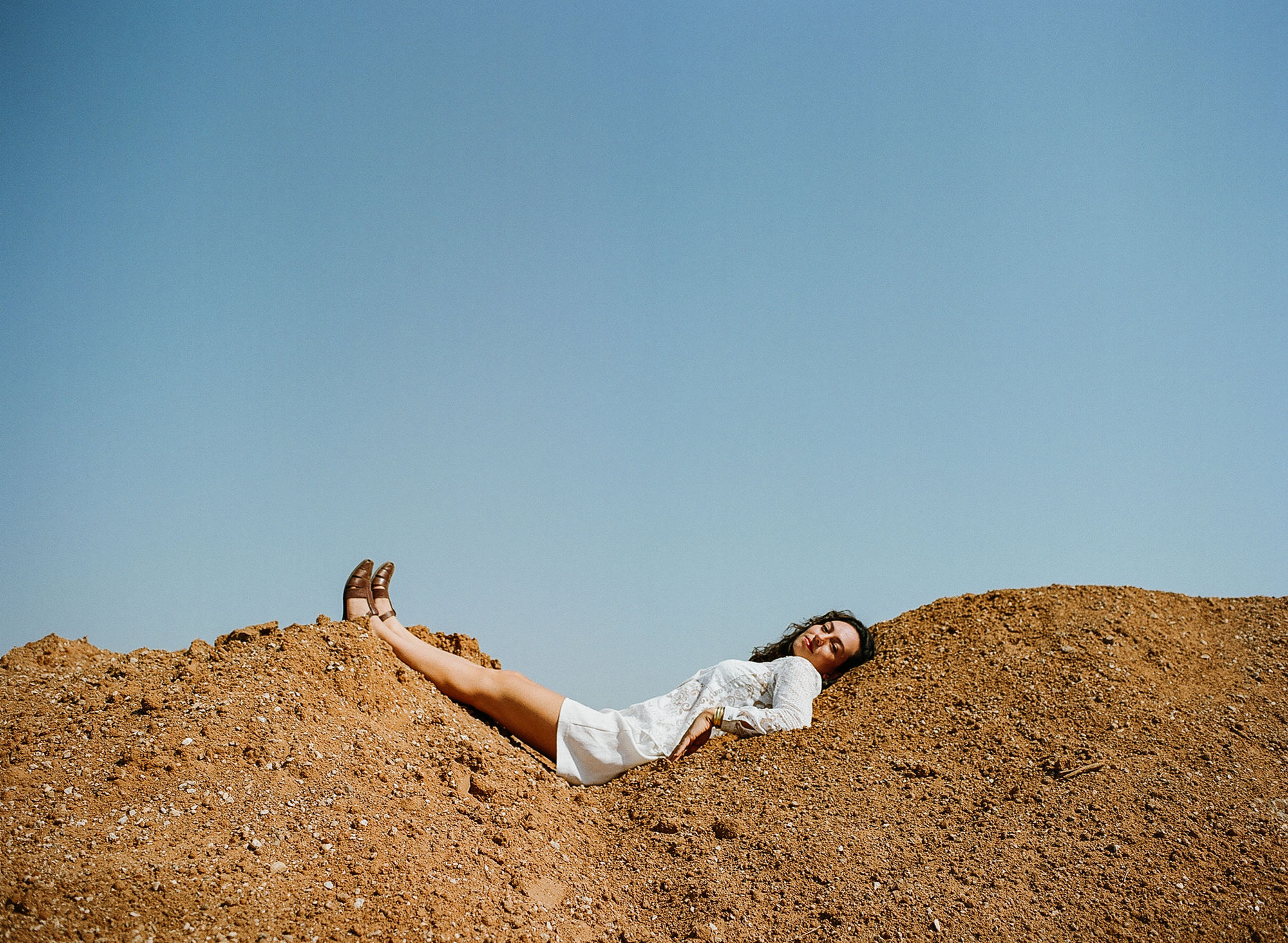 דניאל רובין שוכבת על תל עפר מתחת לשמיים כחולים